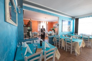 Kellner serviert eine Flasche Wein zwischen den gedeckten Tischen im Innenbereich des griechischen Restaurants Mykonos am